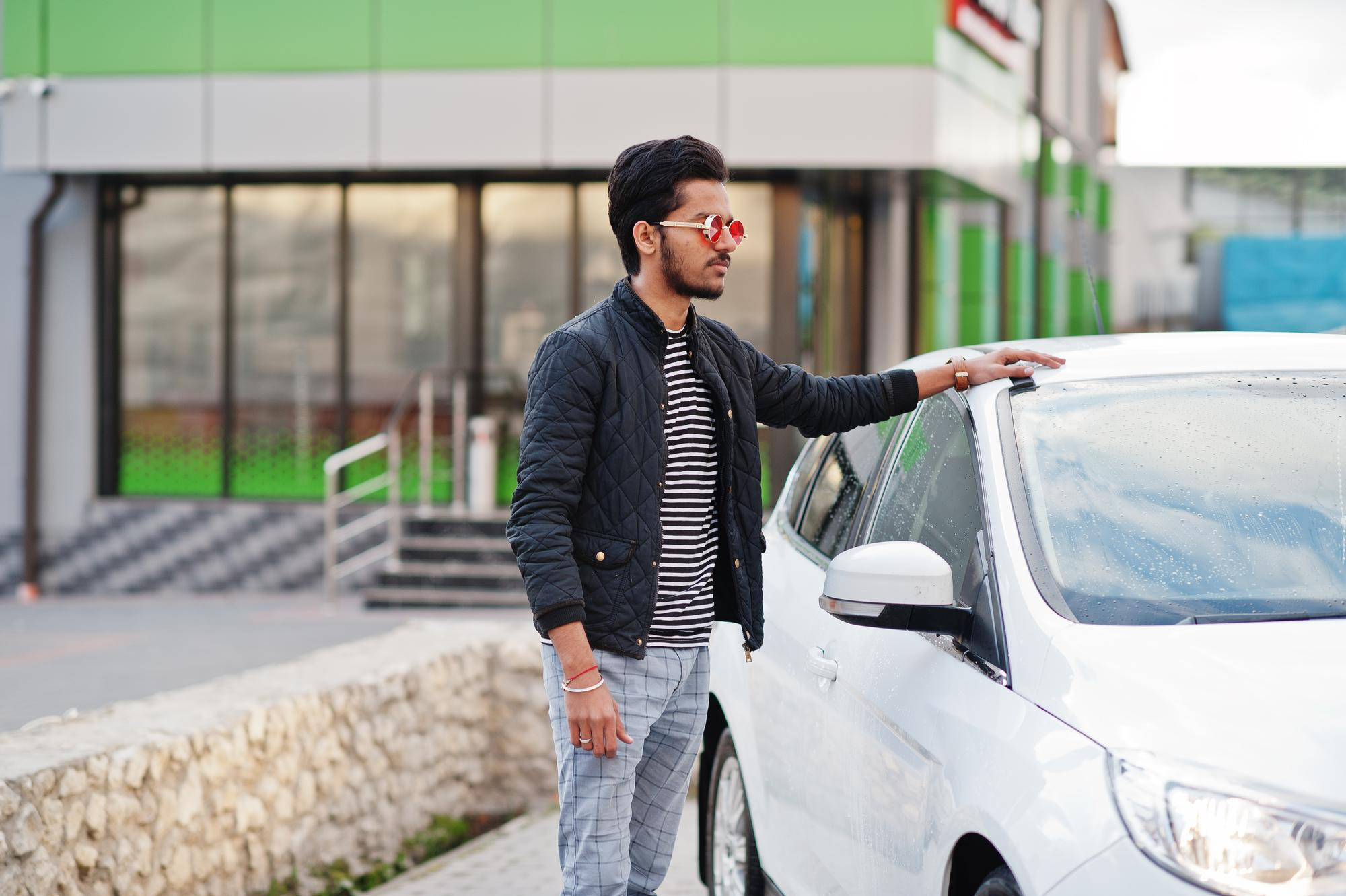A young person standing while holding the roof of a car.