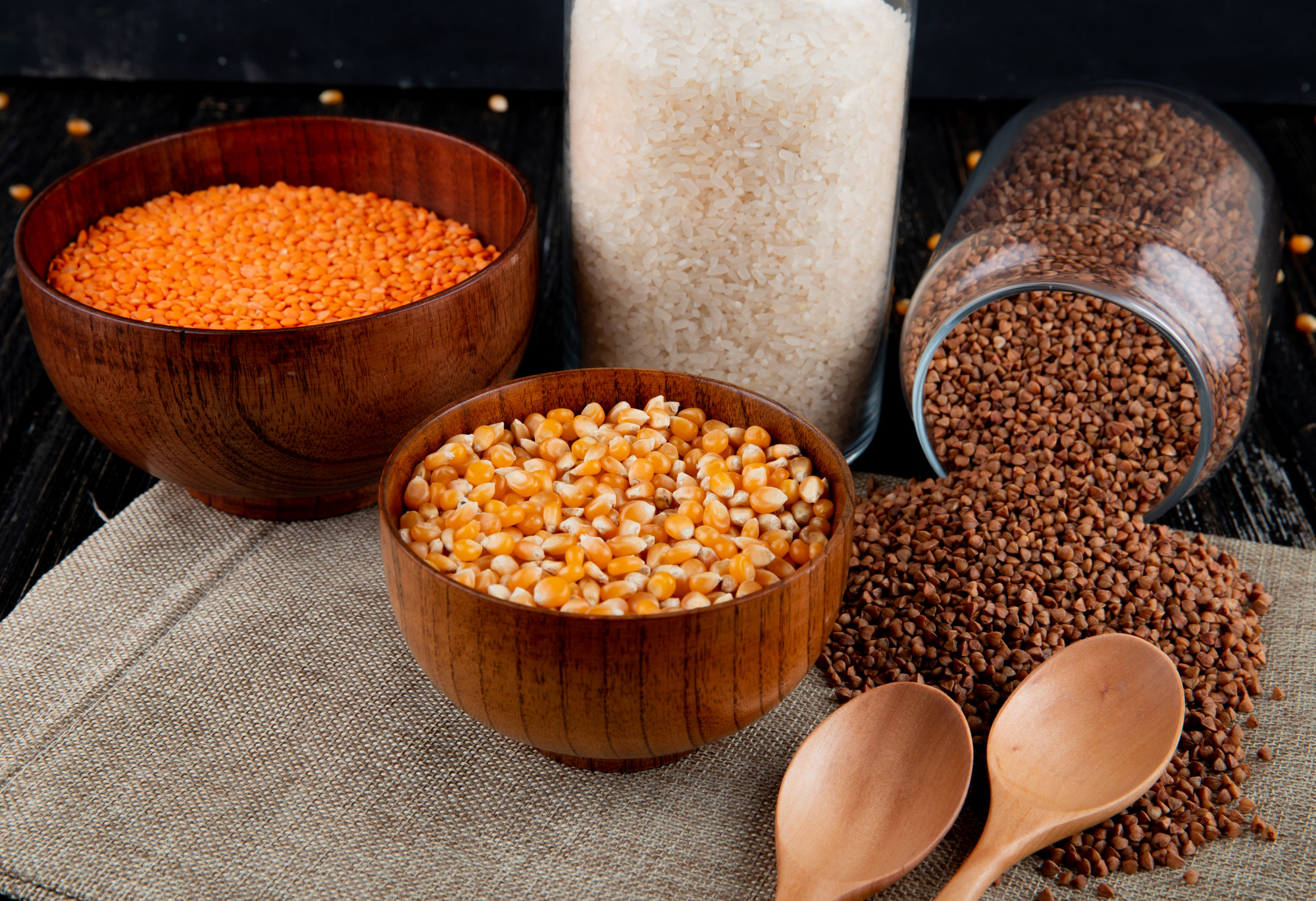 Assortment of millets and grains in wooden bowls and glass jars with wooden spoons, highlighting the benefits of millets