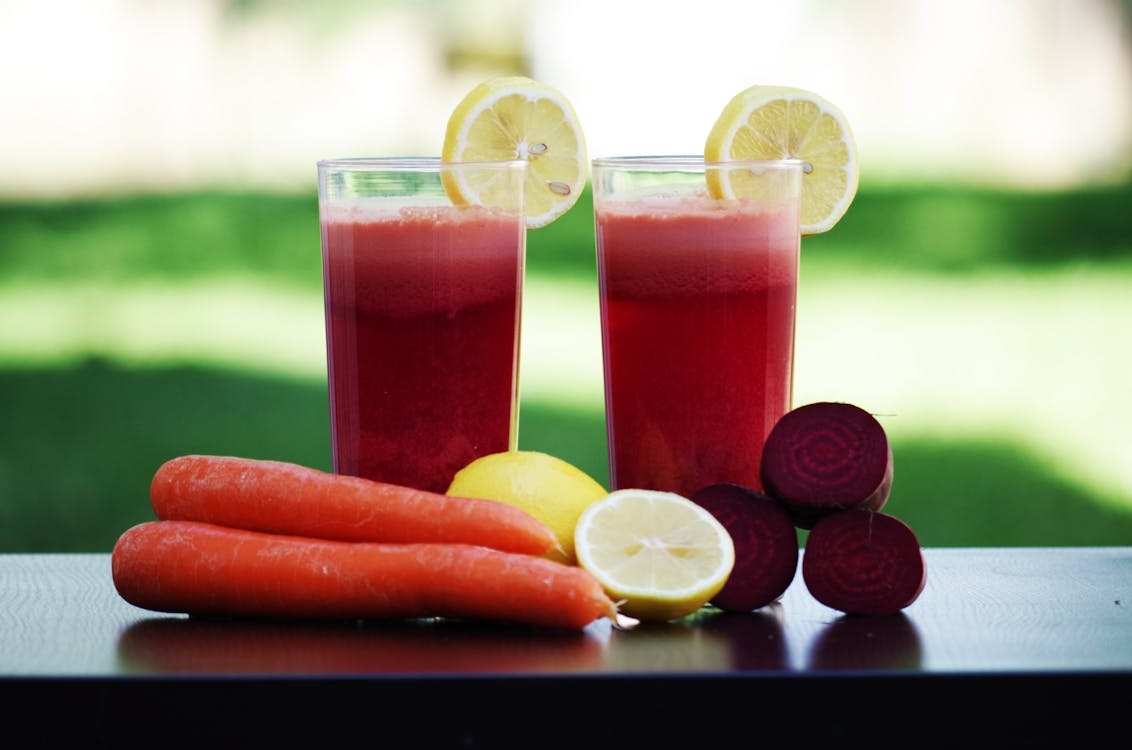Beetroot and carrot juice in a glass, surrounded by raw beetroots and carrots.