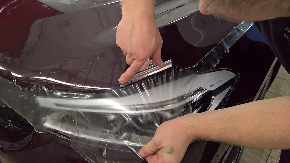 A car stylist seen installing anti-gravel film on the hood of a BMW GT6.