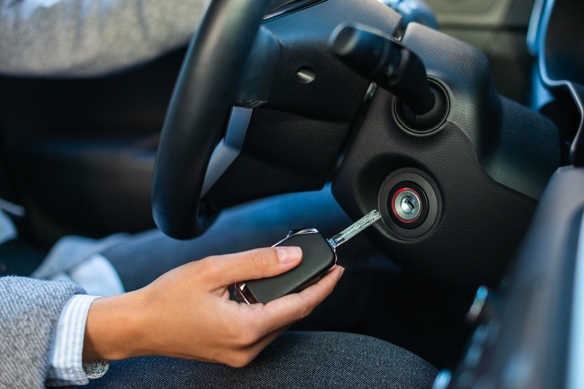 Person in driver's seat holding a car key and attempting to insert it into the ignition slot, illustrating common car starting problems.