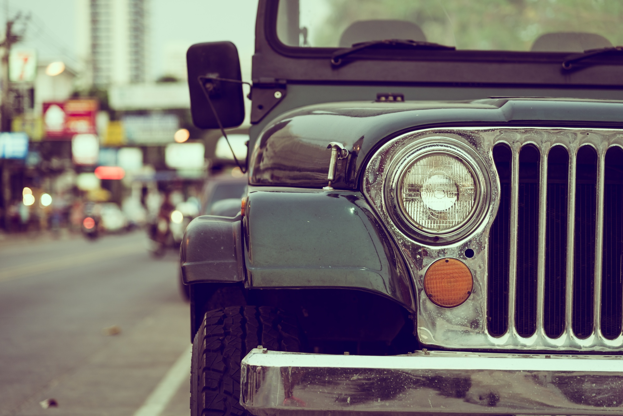 Close-up of the front of an old green off-road jeep parked on a city street.