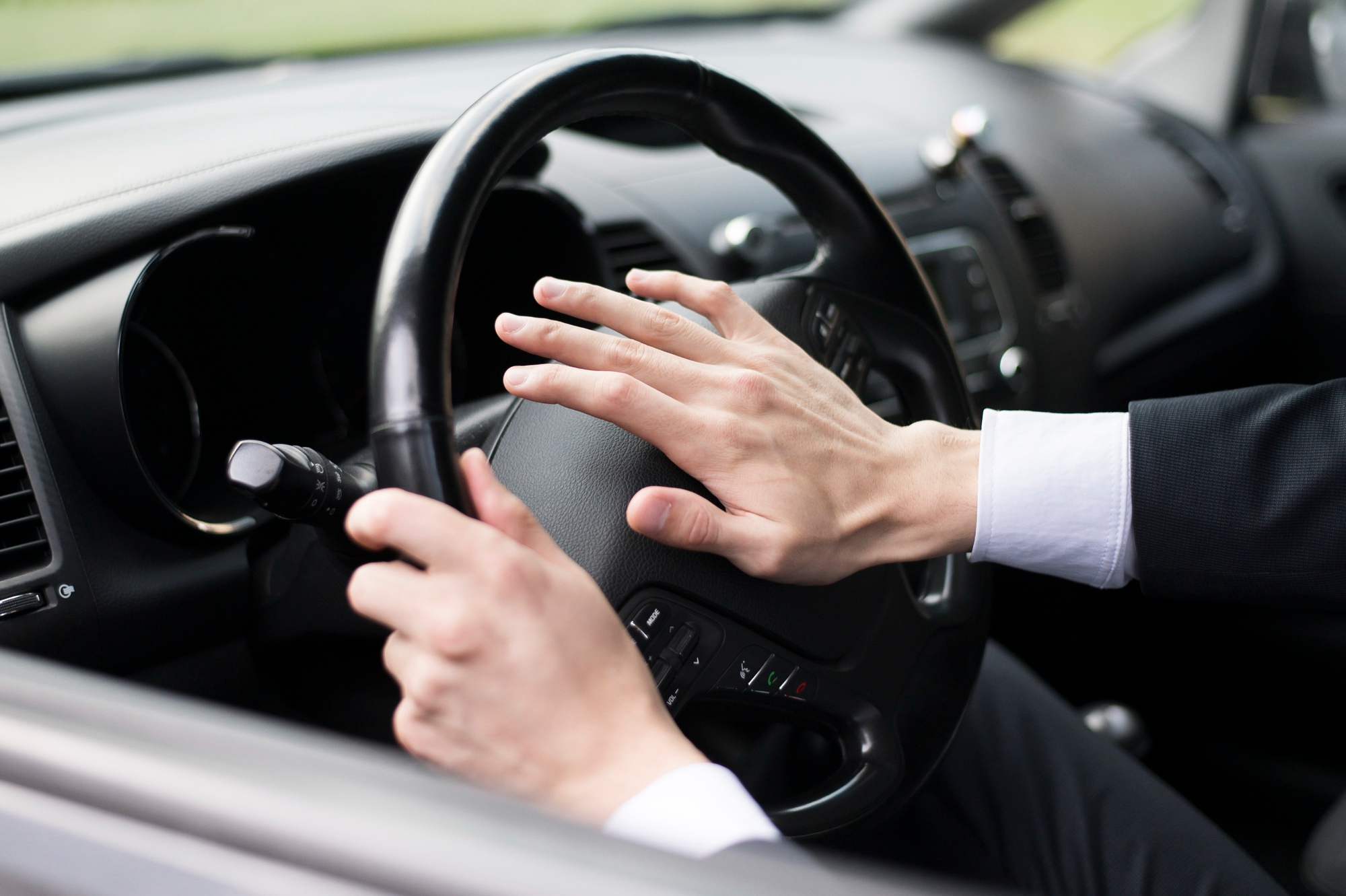 Driver pressing the car horn on a steering wheel while seated inside a vehicle.