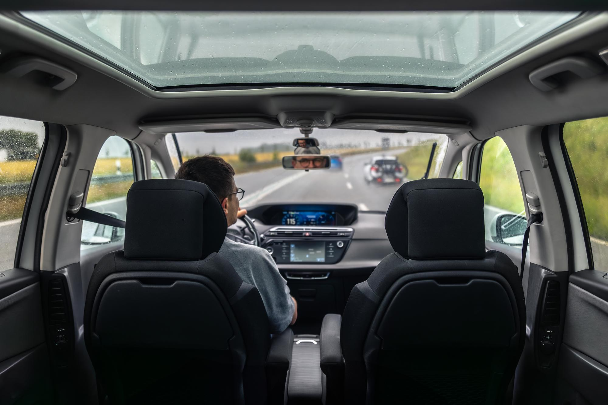 Interior view of a car from the rear seats showing a driver on a highway.