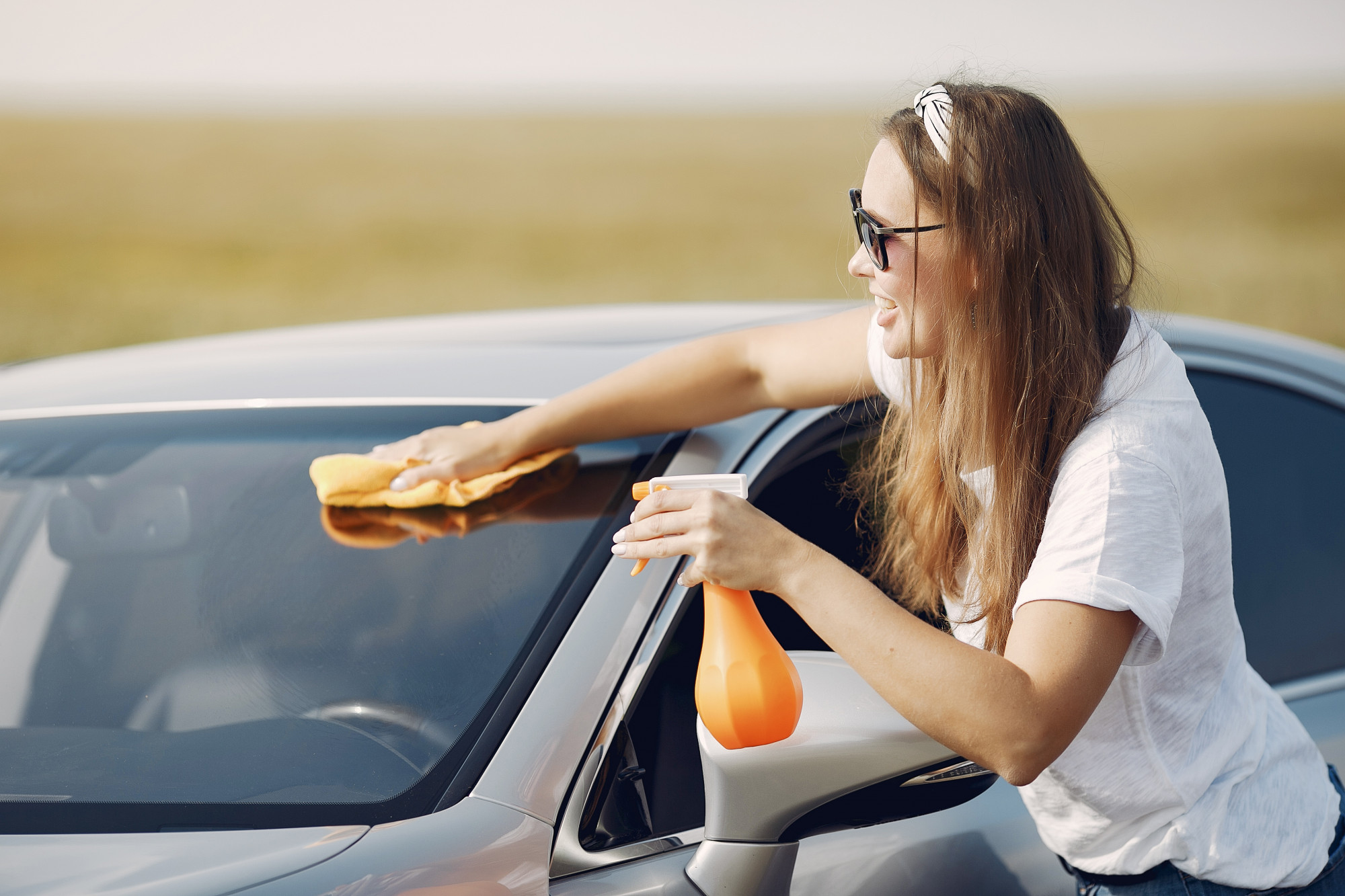 A woman is seen cleaning her car windshield.