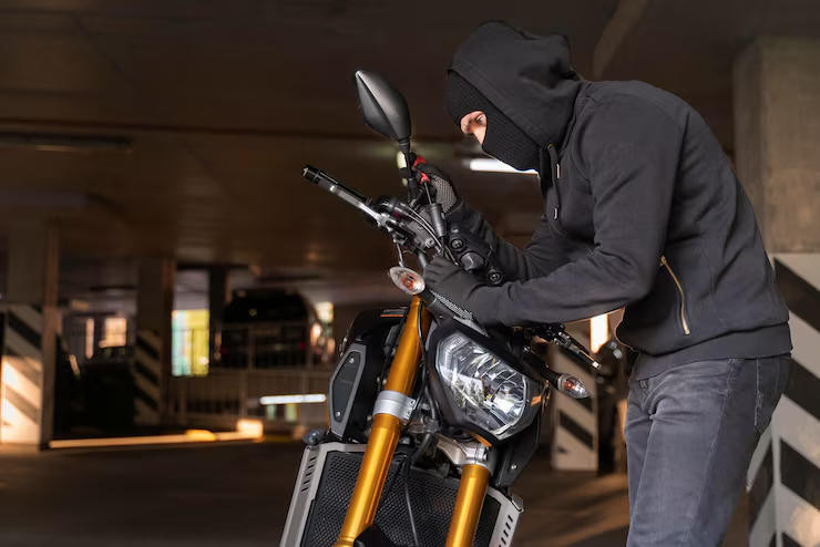A person wearing a black hoodie is attempting to steal a motorcycle in a dimly lit underground parking garage, highlighting the risk of motorcycle theft.