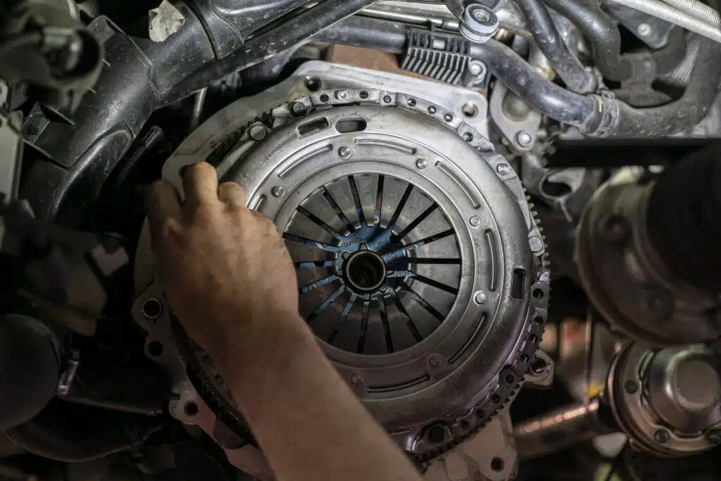 A close-up photograph depicting a mechanic working on a manual transmission car's clutch assembly.
