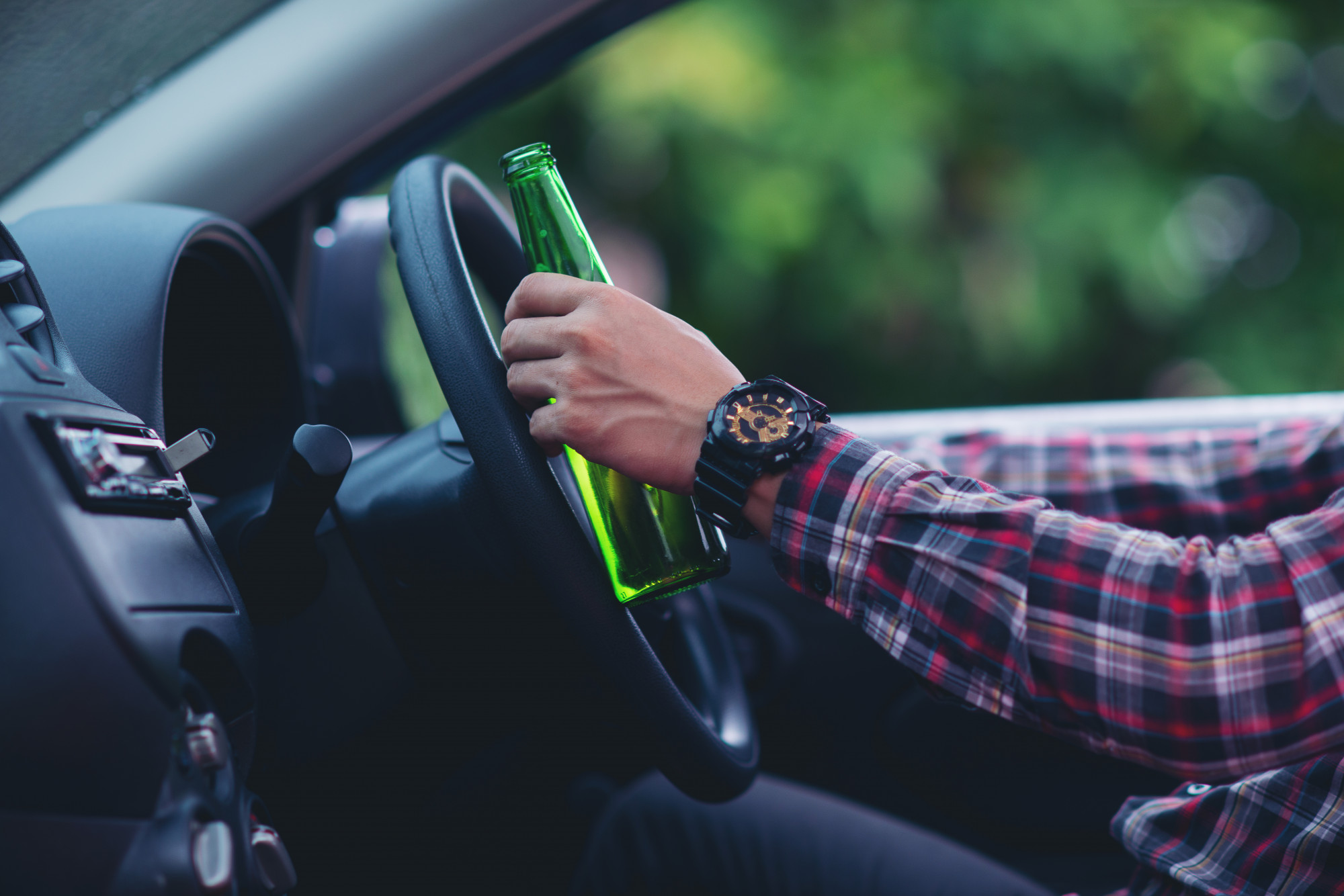 A man holding a beer bottle while driving.