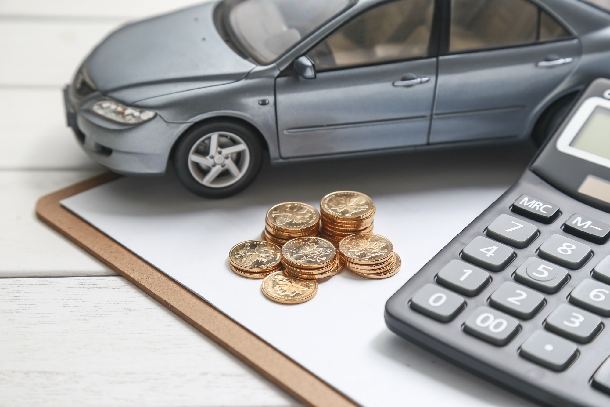 A detailed miniature car model placed beside a calculator and coins on a white table