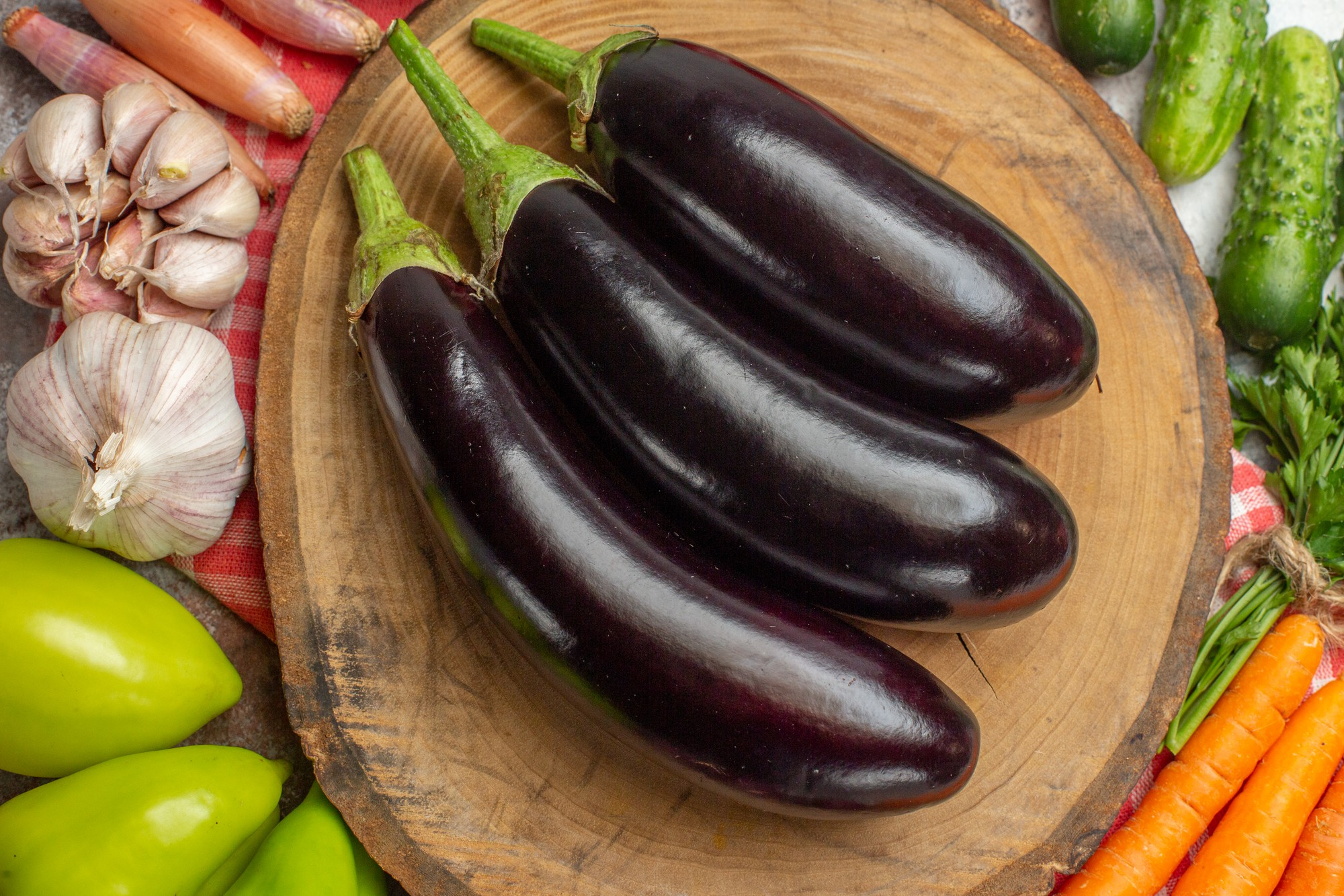 Three glossy purple eggplants resting on a wooden board.