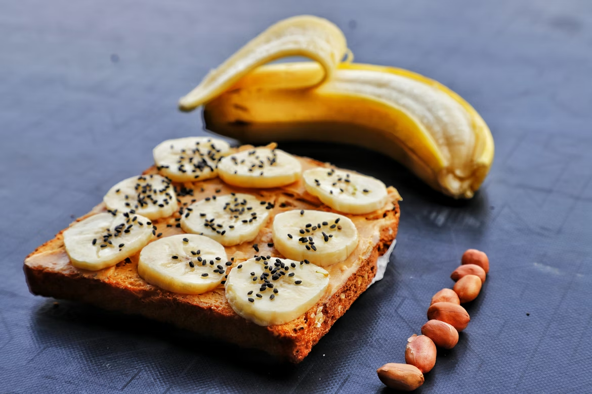 Whole grain peanut butter toast topped with bananas and black sesame seeds, along with peanuts; a snack that naturally provides vitamin B1.x