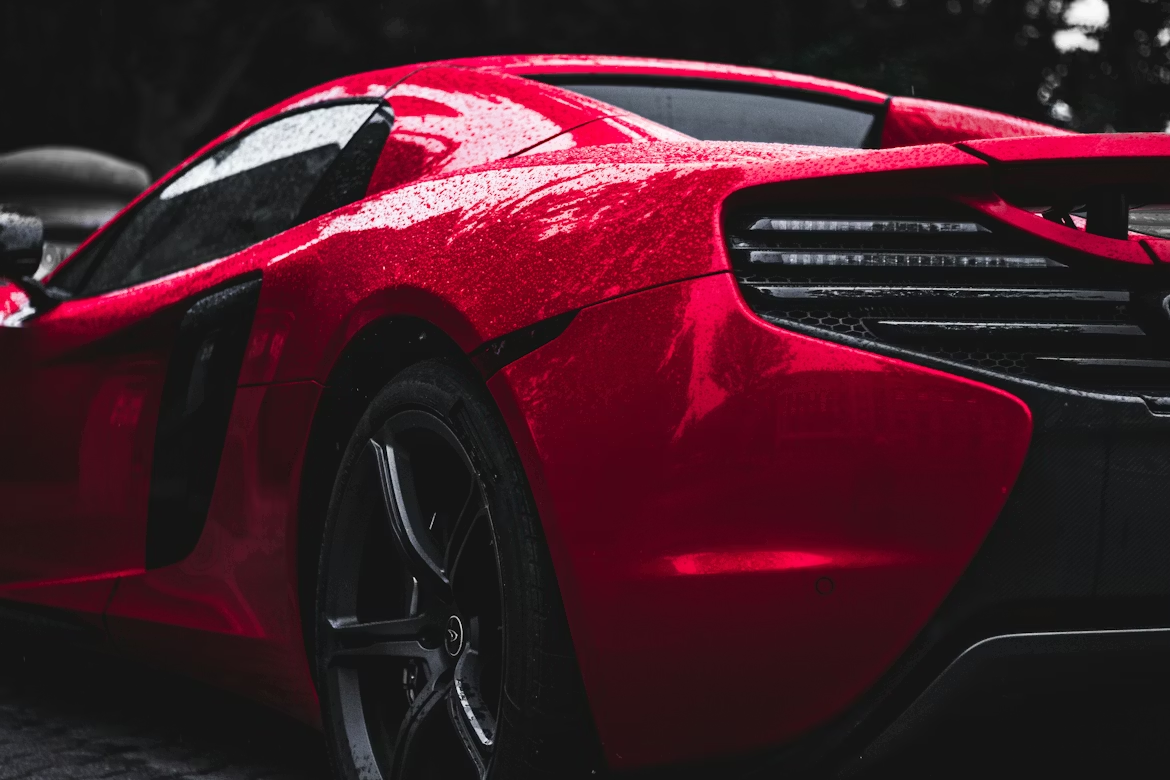 Red car rear view, wet glossy finish, dark moody background.