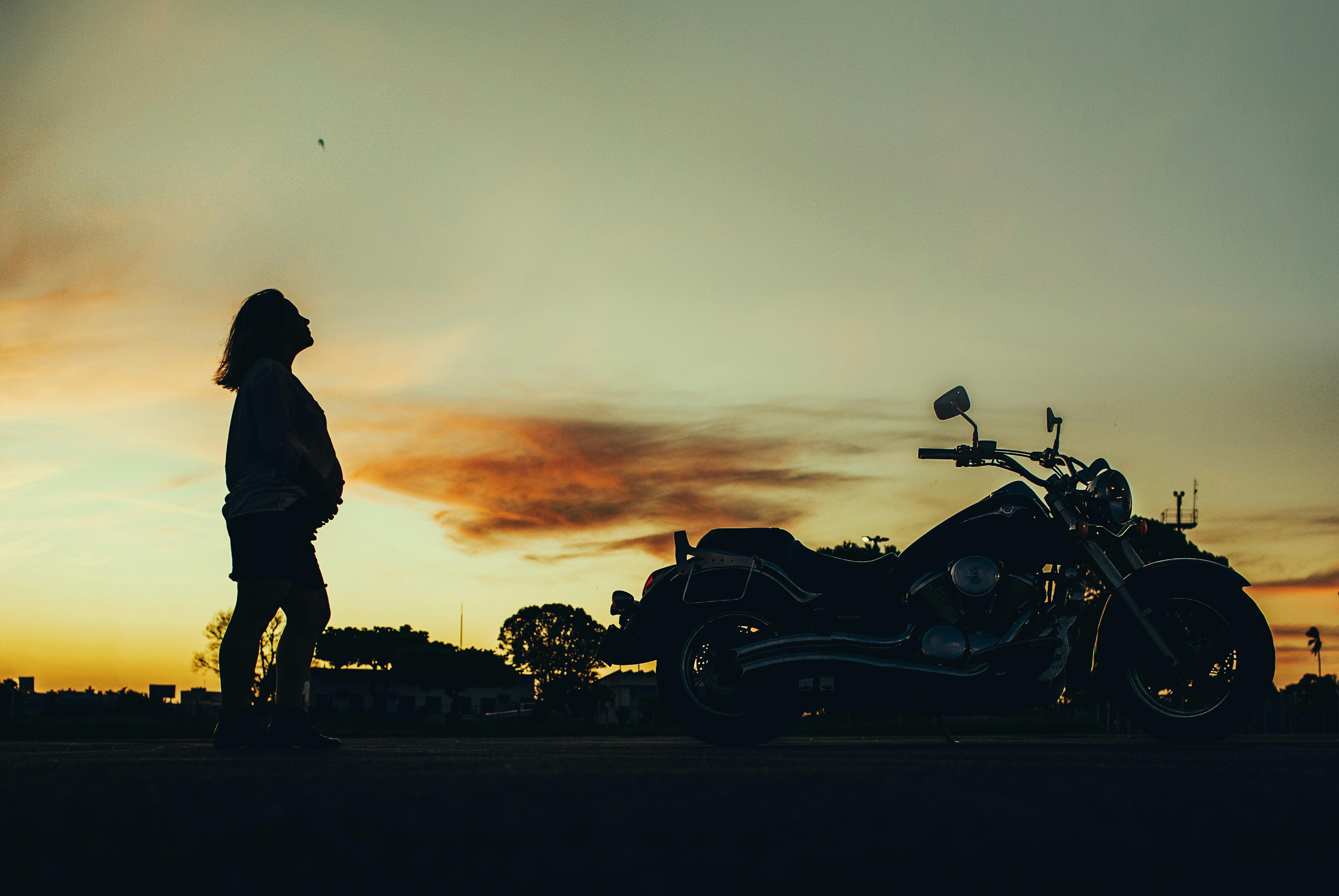Silhouette of a pregnant woman near a motorcycle during sunset.